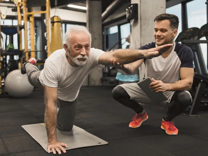 Idoso com treinador fazendo exercícios na academia.