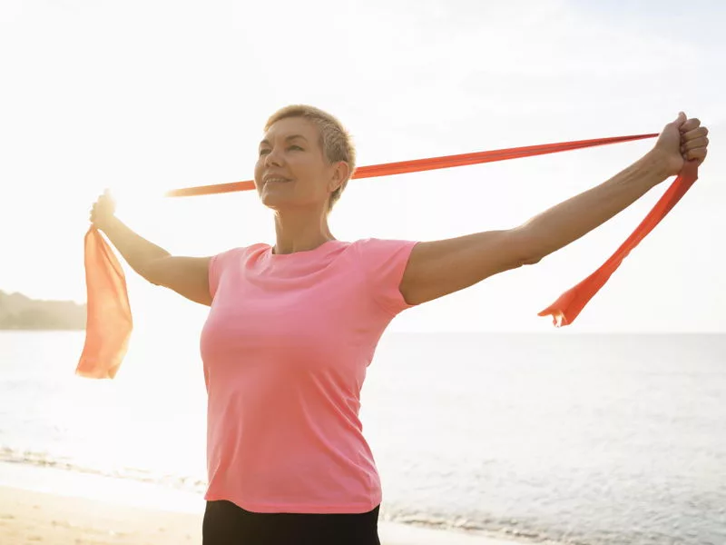 Mulher na praia fazendo exercísios com aspecto feliz e otimista.